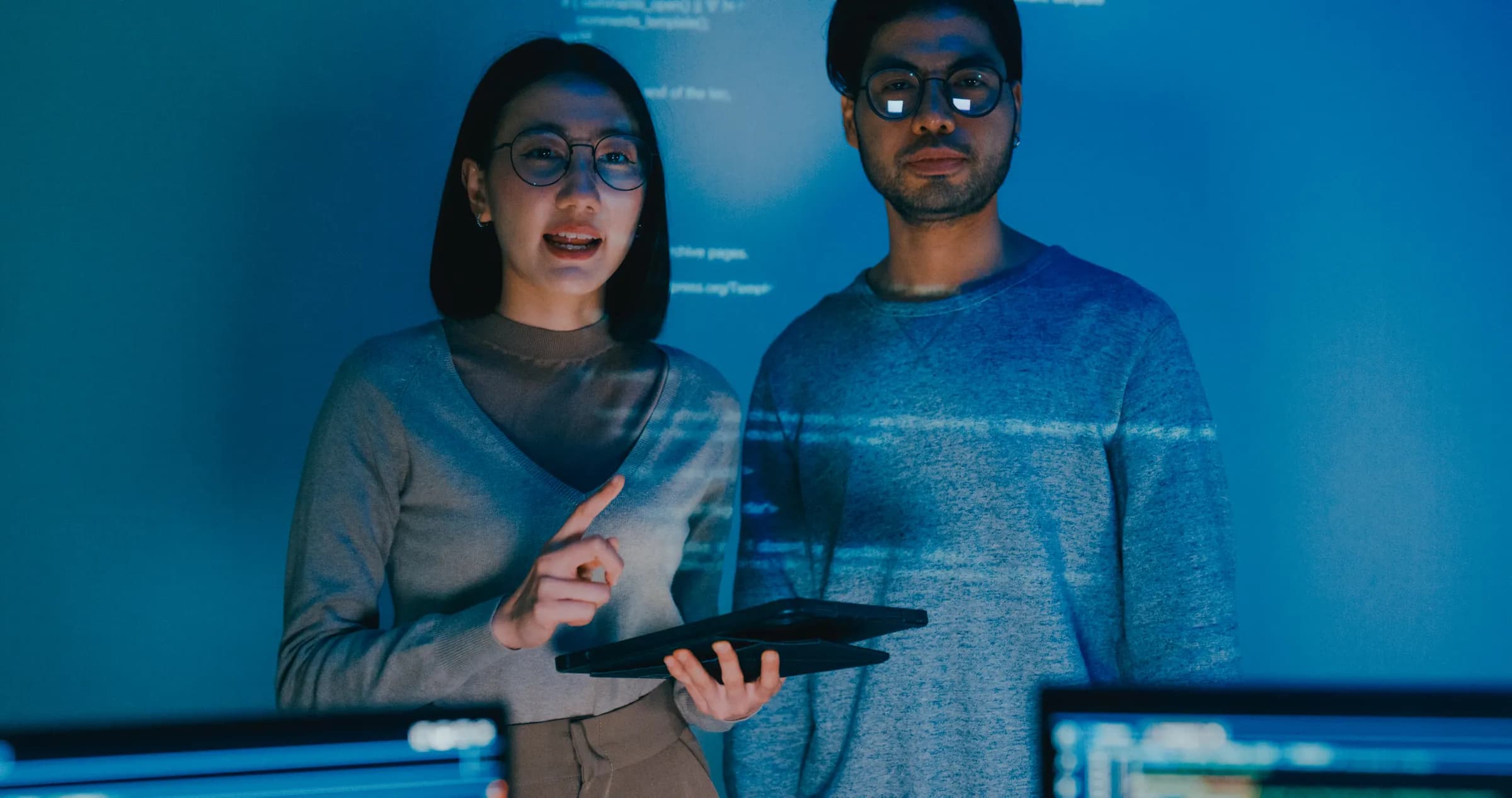Two engineers reviewing code projected in a dark room